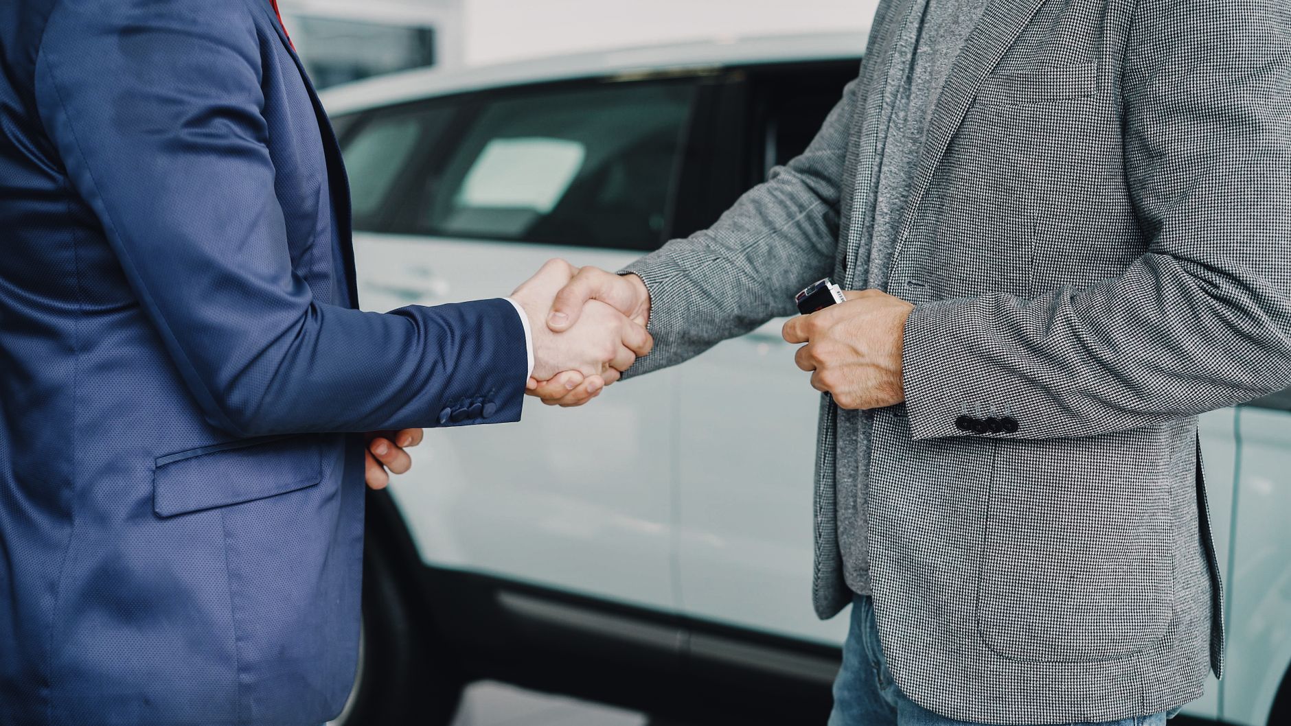 Aperto de mãos entre vendedor e comprador ao lado de um carro